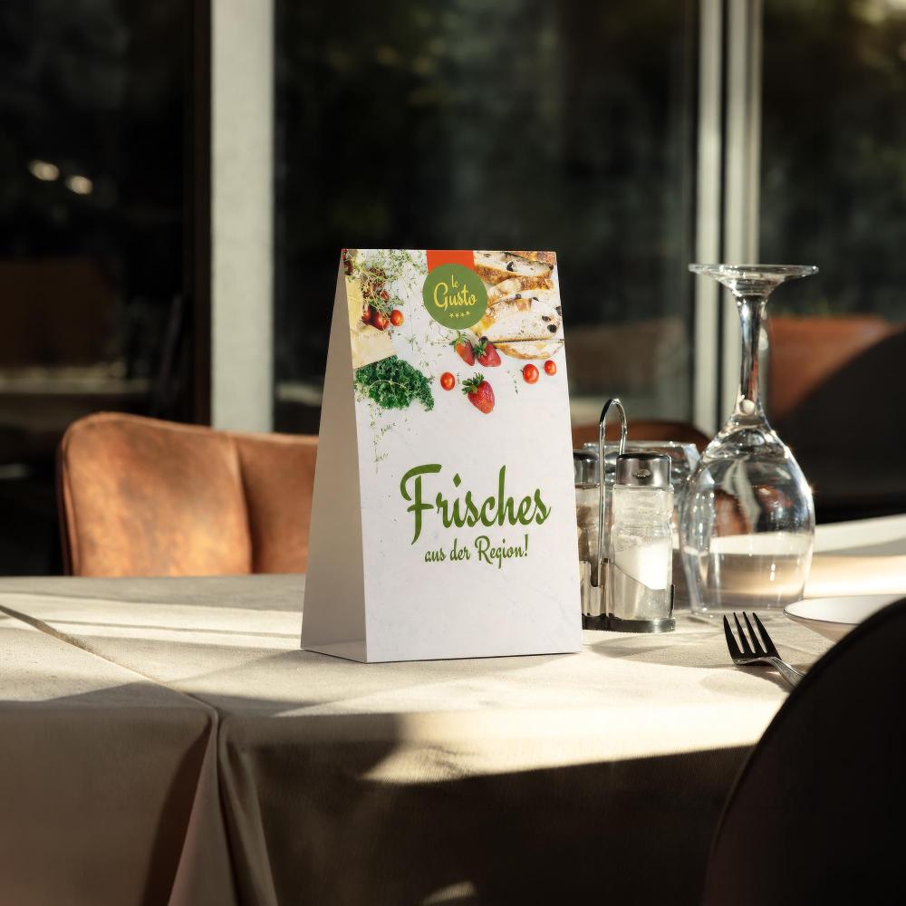 Bedruckter klassischer Tischaufsteller im Format 98 × 162 mm auf einem gedeckten Restauranttisch