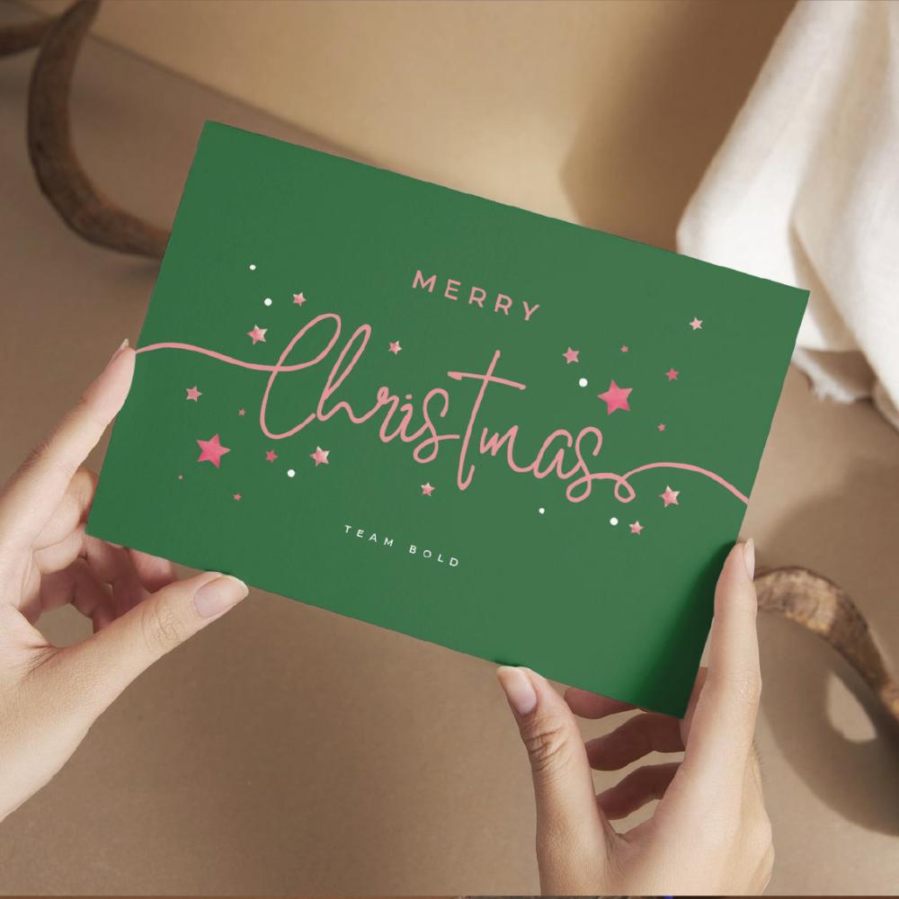 Gedruckte Weihnachtskarte im Format A6 wird von zwei Händen getragen. Weihnachtliche Stimmung.